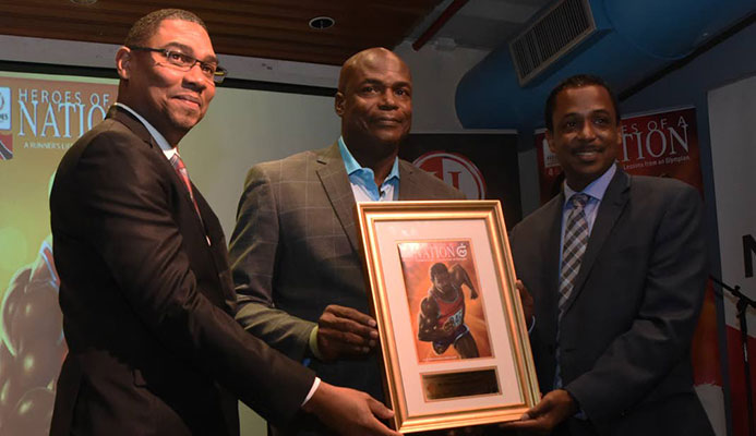NGC’s vice president of operations Ronald Adams, left, and chairman of the Heroes Foundation Philip Julien, right, present Olympic 100m gold medallist Hasely Crawford with a framed copy of the first edition of the A Runner’s Life - Lessons from an Olympian, at National Library, Port of Spain, on Thursday. PHOTO BY KERWIN PIERRE