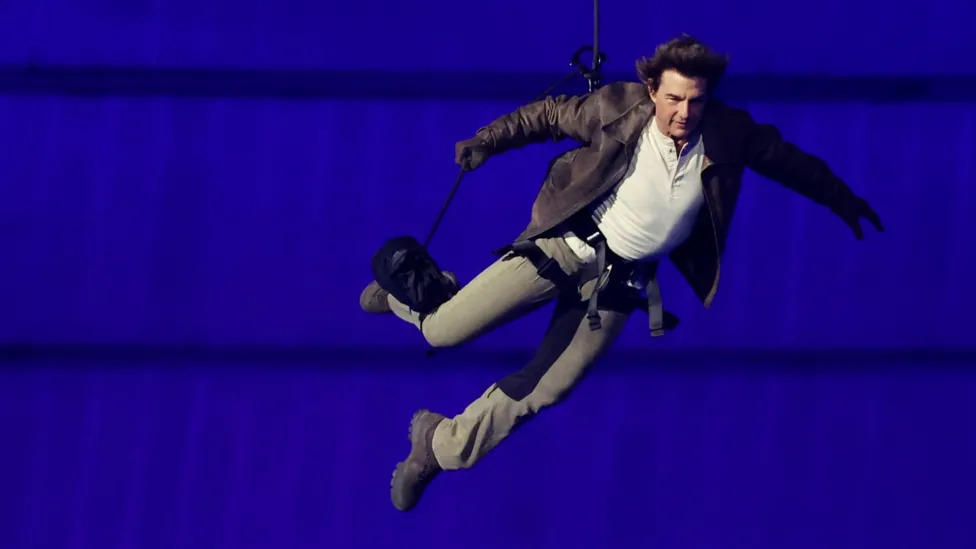 Actor Tom Cruise descended from the roof of the stadium to collect the Olympic flag, before departing on a motorcycle to begin its journey across the Atlantic (Image obtained at bbc.com)